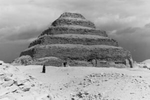 The Step Pyramid of Djoser at Saqqara, Egypt, viewed from the base beneath a cloudy sky.